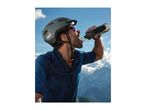 Cyclist in helmet and sunglasses drinking from a water bottle with mountains in the background.