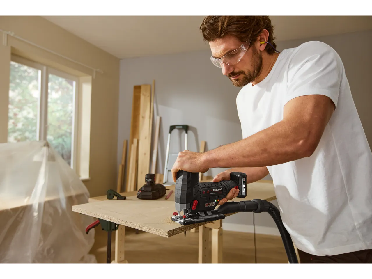 A man uses a Parkside jigsaw with vacuum attachment to cut a piece of wood.