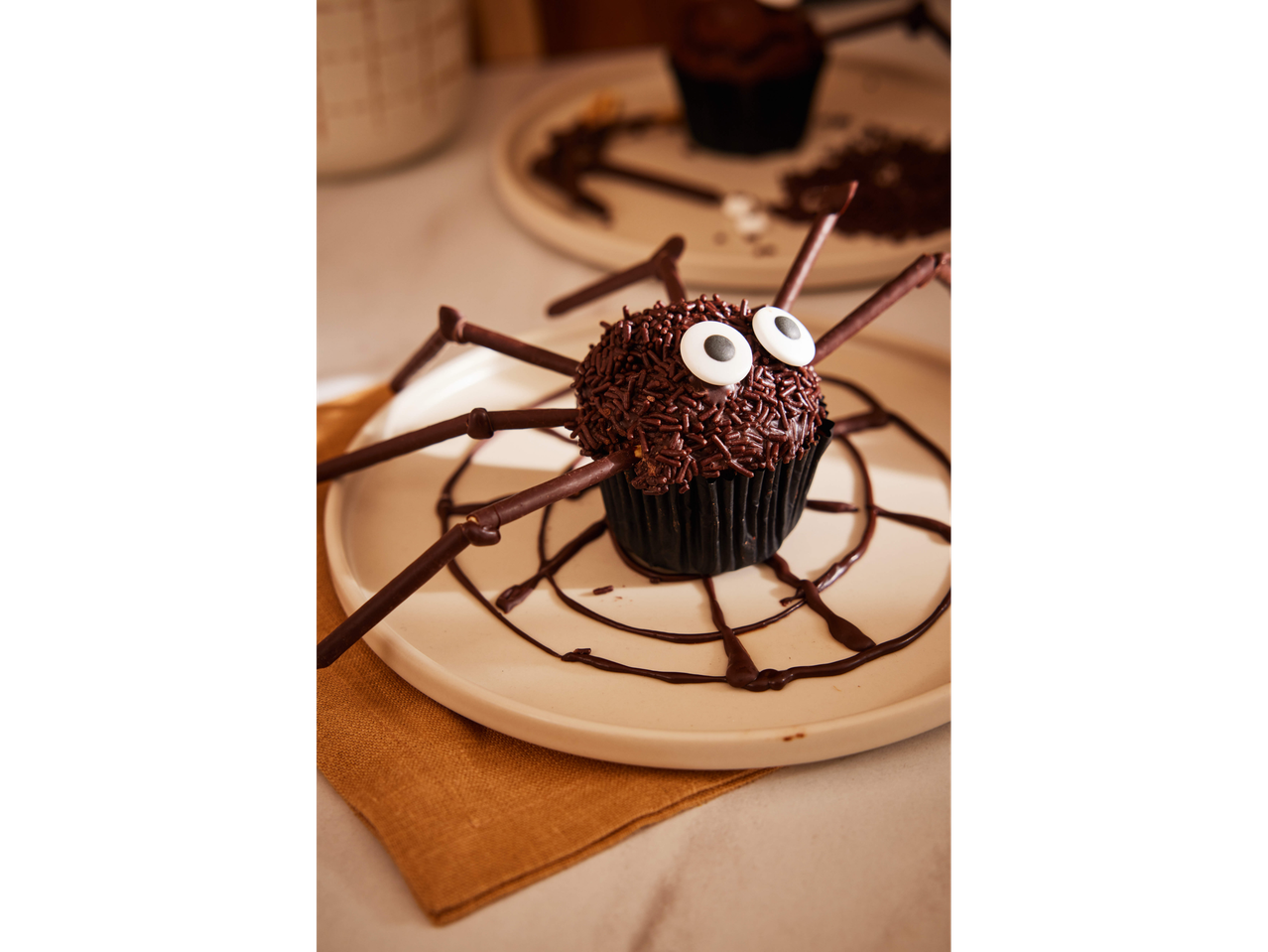 Brioșă-păianjen de Halloween cu ciocolată și ochi de bomboane pe o farfurie