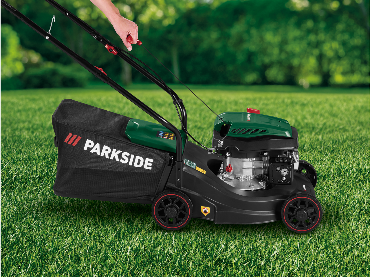Person mowing a green lawn with a black and green petrol lawnmower.
