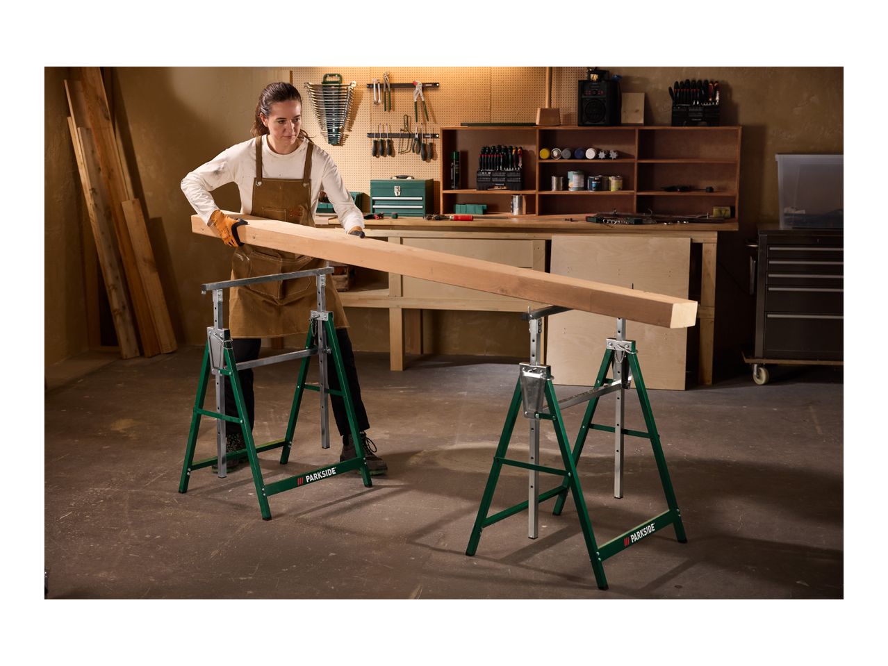 Woman in a workshop placing a wooden beam on two green saw horses.