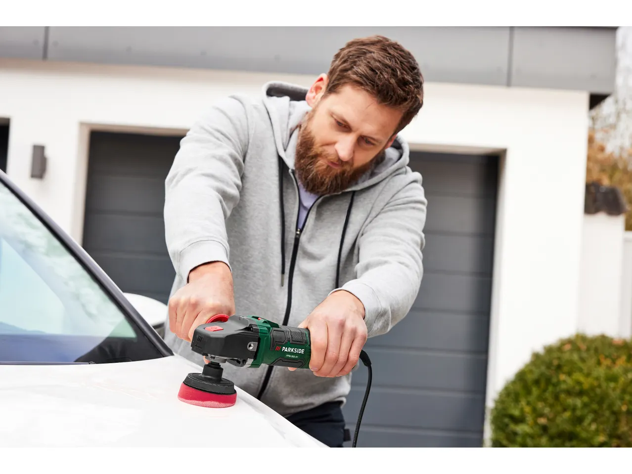 Un uomo utilizza una lucidatrice PARKSIDE® per lucidare un'auto.