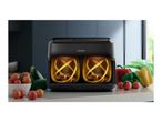 Black dual-basket air fryer with glowing interiors on a kitchen counter with vegetables.