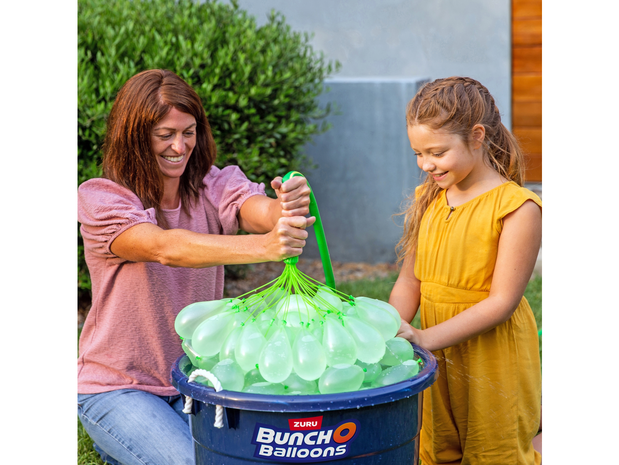 A woman and child filling Zuru Bunch O Balloons water balloons in a blue bucket.
