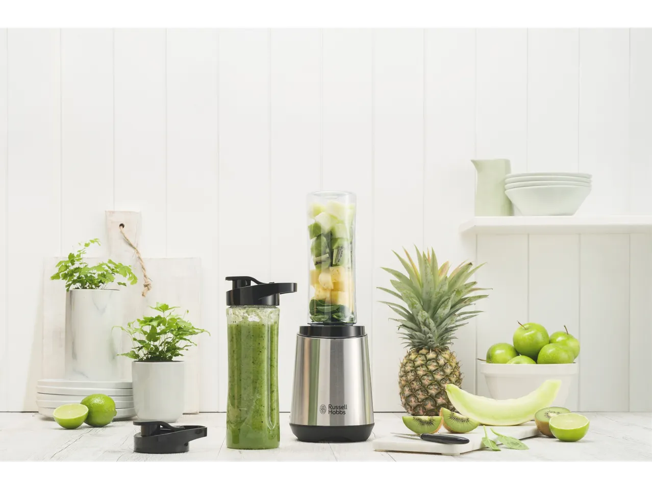 Blender Russell Hobbs cu smoothie verde și fructe proaspete pe un blat deschis.