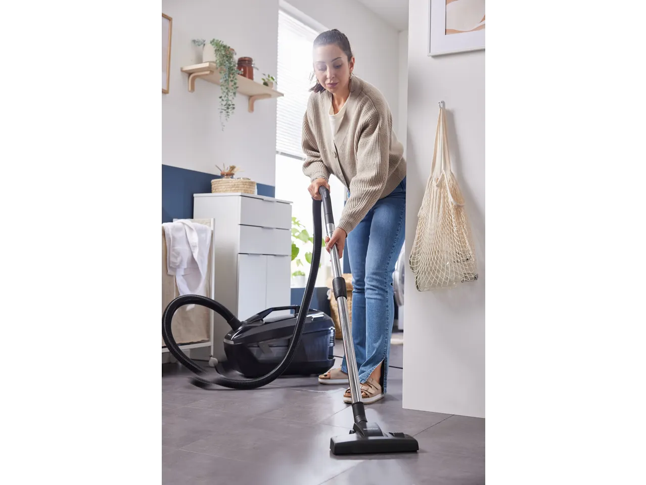 Mulher a aspirar com um aspirador com filtro de água Silvercrest® numa divisão moderna.