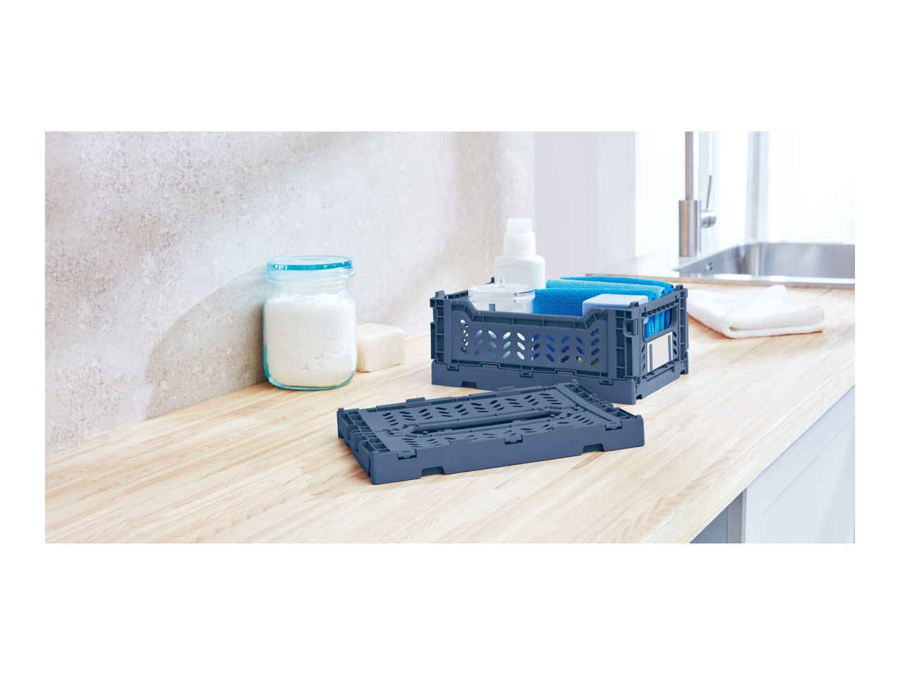 Two foldable storage crates, one filled with cleaning supplies, on a wooden countertop.