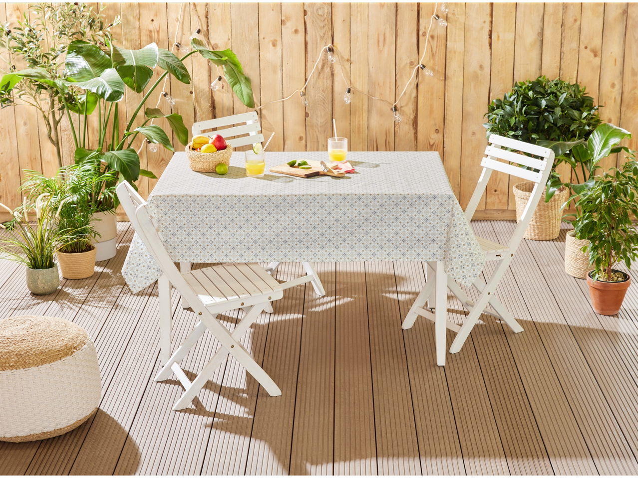 White folding chairs and table, patterned tablecloth, potted plants.