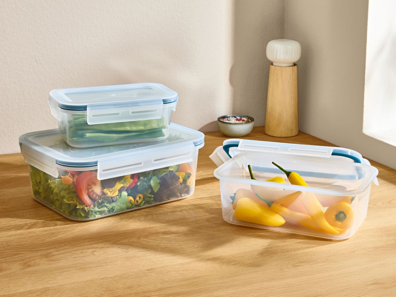 Clear food storage containers with fresh salad, green beans, and yellow peppers on a wooden table.