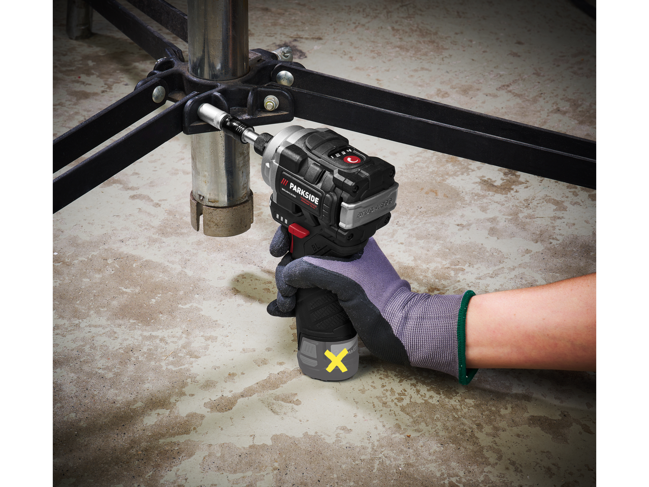 Una mano guantata usa un Avvitatore a percussione Parkside PERFORMANCE® per stringere una vite.