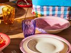 Un tavolo in legno con bicchieri colorati e ciotole rosa e bianche.