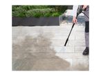 Person cleaning patio paving with a pressure washer, showing before and after sections.
