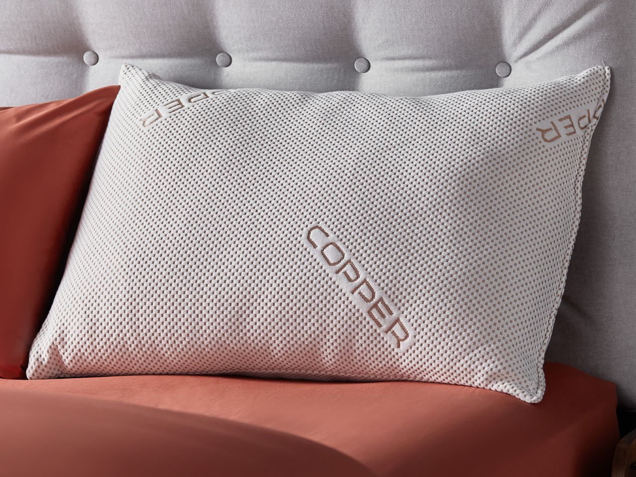 Copper Pillow resting on a terracotta colored bedsheet.