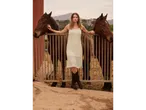 Femeie în rochie croșetată și cizme de cowboy cu doi cai.