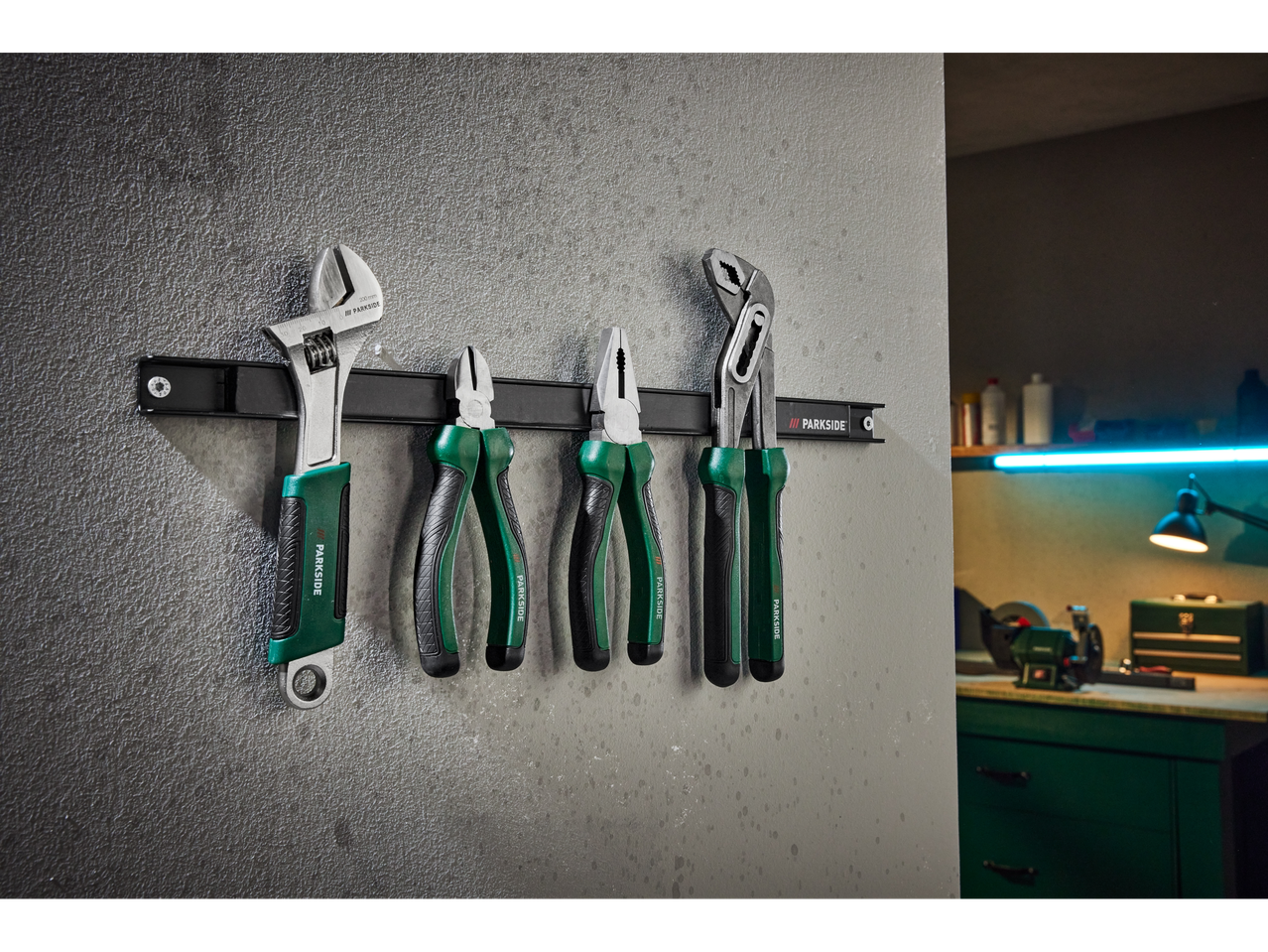 Werkzeugset mit verstellbarem Schraubenschlüssel und Zangen, die an einer Magnetleiste in einer Werkstatt hängen.