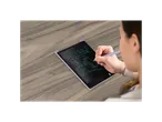 A woman uses a stylus to draw on a purple LCD writing tablet on a wooden desk.
