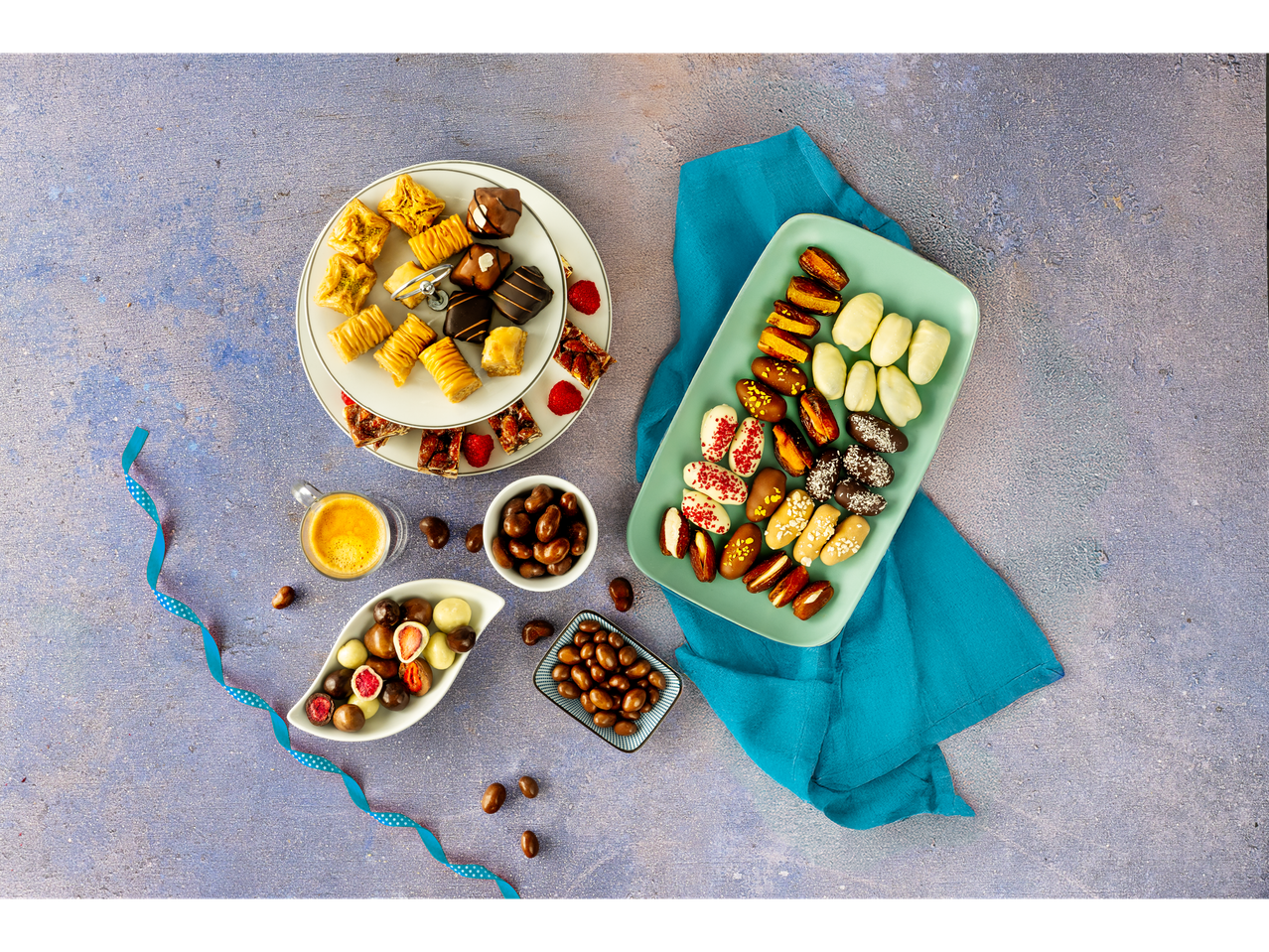Assortment of baklava, chocolates, dates, and coffee on a textured blue surface.