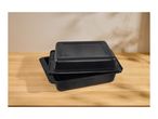 Two black roasting pans, one stacked on top of the other, on a wooden surface.