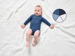 A baby in a blue bodysuit lying on a white knitted blanket, with a color palette.
