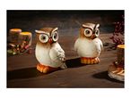 Two ceramic owl figurines with autumn decorations and candles on a wooden table.