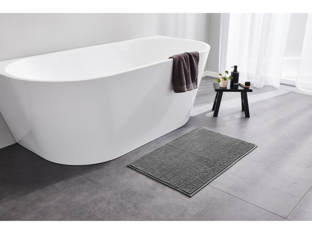 LIVARNO home gray bath mat on a tiled floor next to a white bathtub.