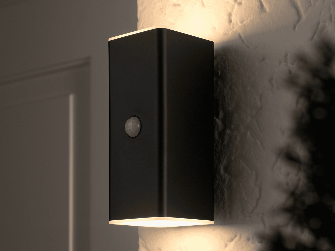Schwarze Wandleuchte mit Bewegungssensor, die warmes Licht nach oben und unten abstrahlt.