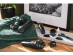 Electric shaver and hair clippers with various attachments, oil, and scissors on a wooden surface.
