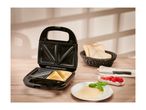 Black sandwich maker with two toasted sandwiches, bread, cheese, and tomatoes on a wooden table.
