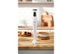 A white SilverCrest immersion blender on a wooden counter with a bowl of soup and ingredients.
