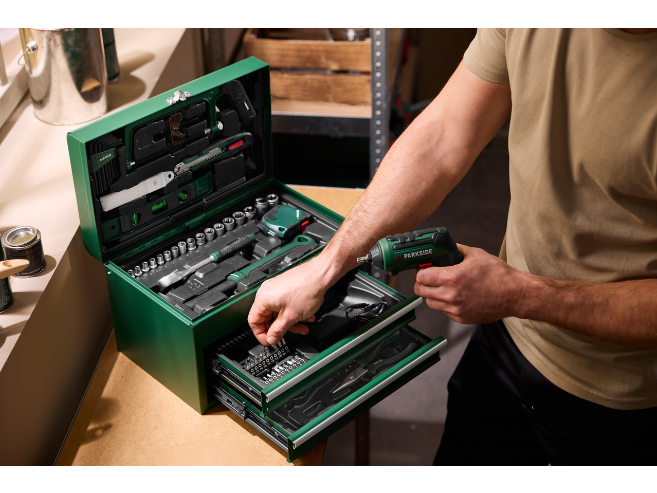 Bărbat luând un burghiu dintr-o cutie de scule verde PARKSIDE cu o șurubelniță fără fir.