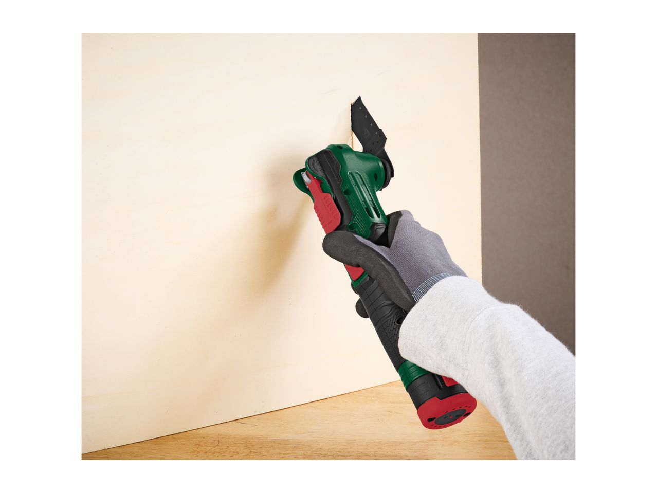 Gloved hand using a multi-tool to cut into a light wooden board.