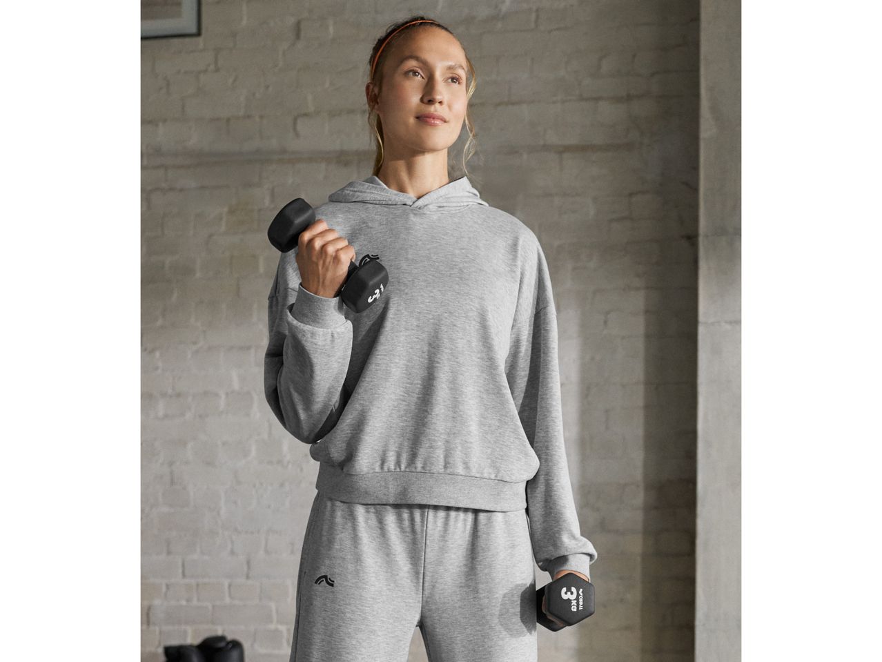 Woman in a gray hoodie and sweatpants holding dumbbells