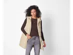 Donna che indossa un gilet lungo beige esmara® sopra una blusa marrone e jeans grigi.