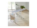 A striped ironing board standing in a bright room next to a laundry basket.