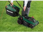 Person attaching the grass collection box to a green PARKSIDE® 1500W Electric Lawnmower on a lawn.