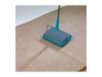 A teal and gray carpet sweeper cleans a beige carpet.