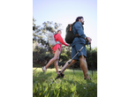Two hikers with CRIVIT hiking backpacks and poles walking through a grassy area.