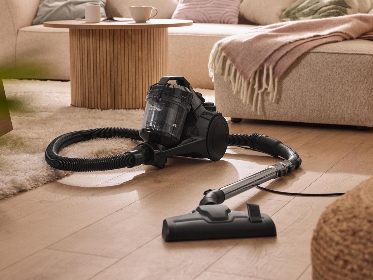 SilverCrest porzsák nélküli porszívó a nappaliban, világos fa padlón és szőnyegen.