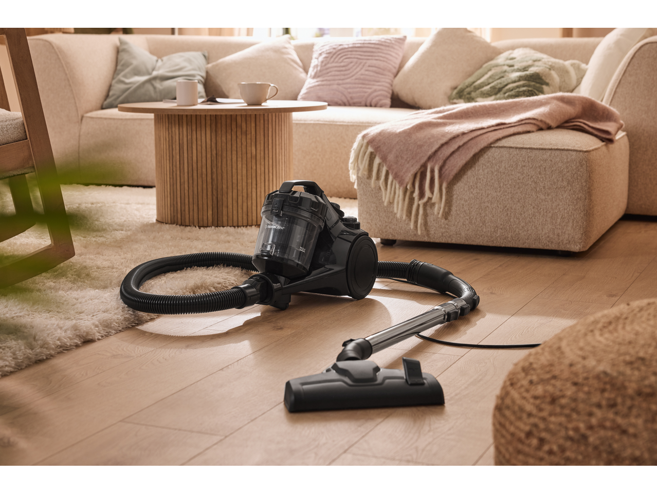 Vacuum cleaner on a wooden floor with a fluffy rug, next to a sofa and coffee table.