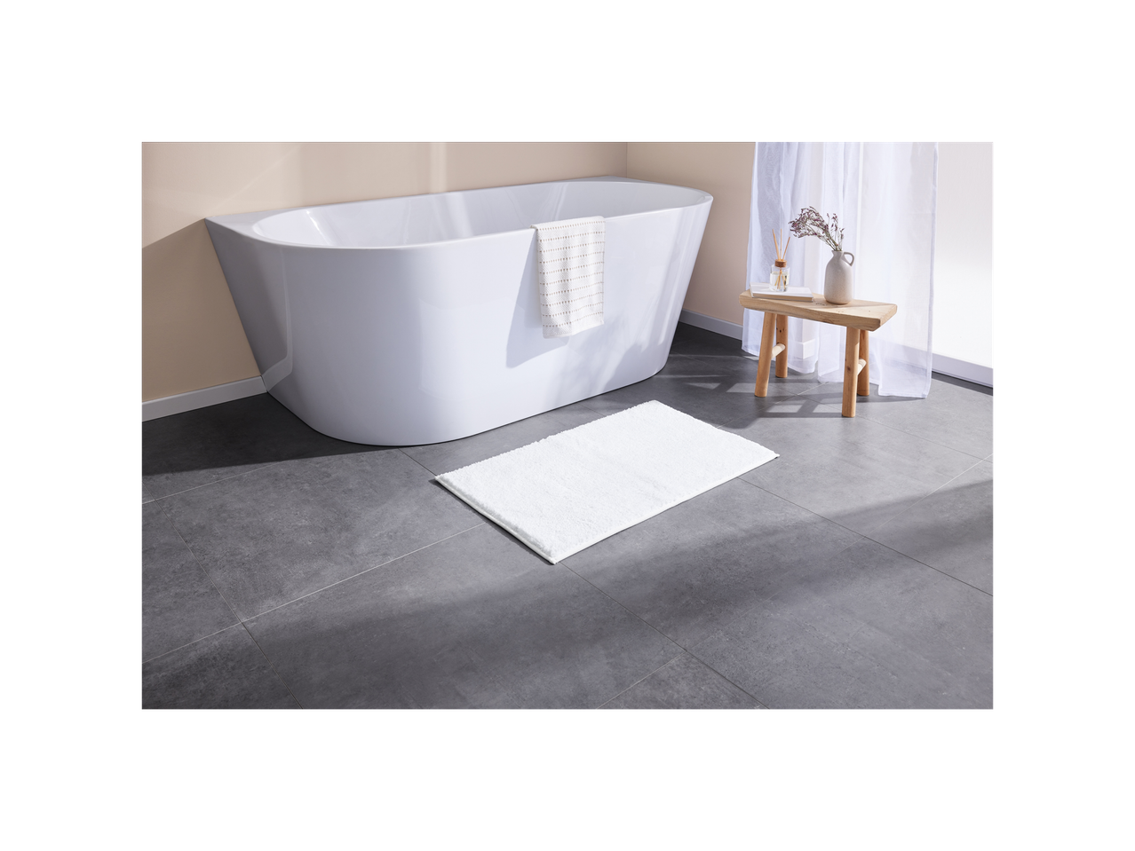 Tappetino da bagno bianco vicino a una vasca da bagno indipendente.