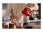 A person using a red hand mixer to whip cream in a bowl next to a bundt cake.