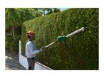 Man in protective gear trimming a tall green hedge with a long-reach hedge trimmer.
