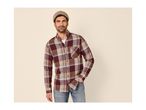 Man in a plaid shirt, jeans, and a beanie, standing with hand in pocket.