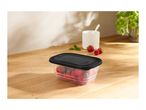 Clear food container with black lid filled with berries on a wooden table.
