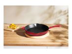Red cast iron skillet on a wooden cutting board with chopped vegetables.