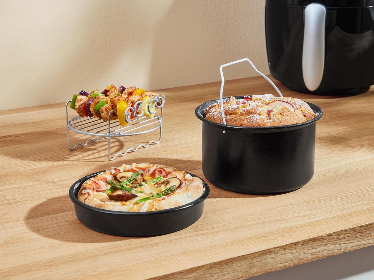 Sütött pizza, gyümölcsös sütemény és grillezett húsgombóc egy air fryer mellett.