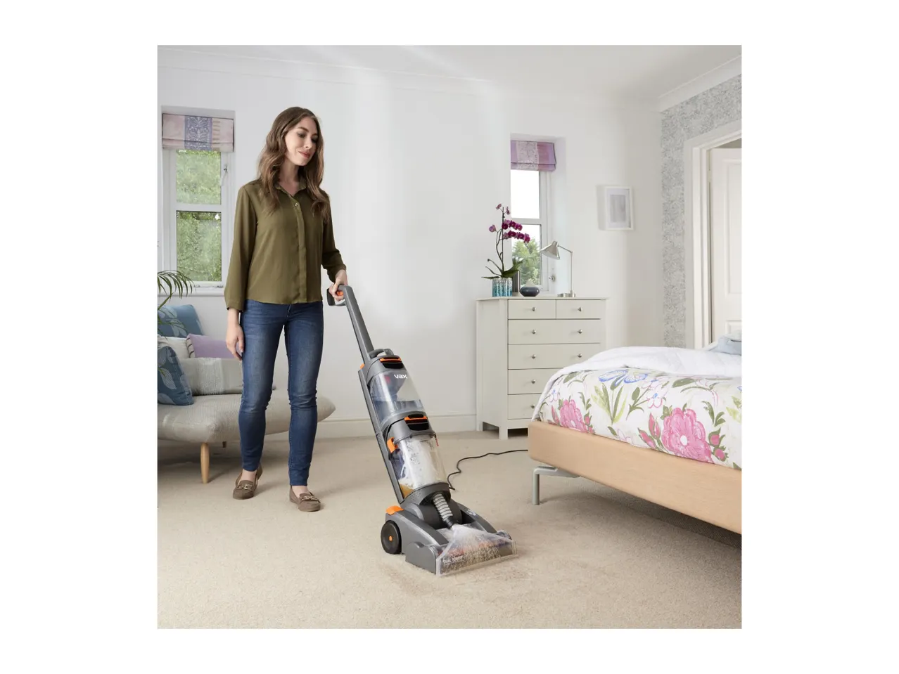 Woman cleaning a carpet with a Vax carpet cleaner in a bedroom.