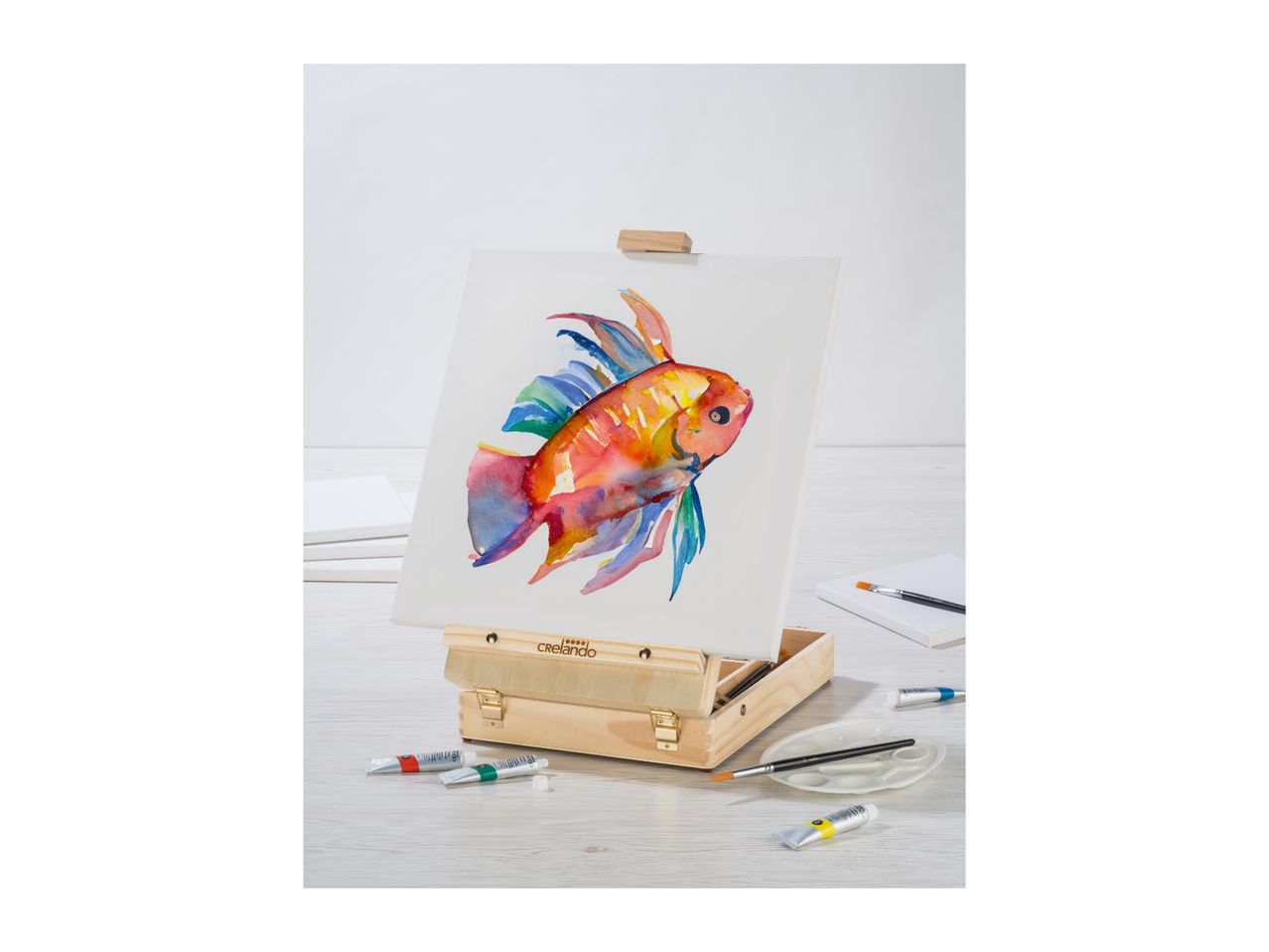 A colorful fish painting on an easel with art supplies.