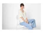 Woman in a cream top and blue jeans sitting on a white chair, smiling.