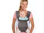 A woman smiles while carrying a baby in a gray baby carrier.